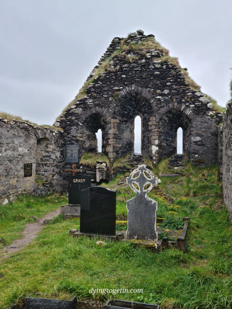 Headstones in the grounds of a old ruined church with three arched windows. One headstone, in black marble, is etched with the name GRADY in gold letters