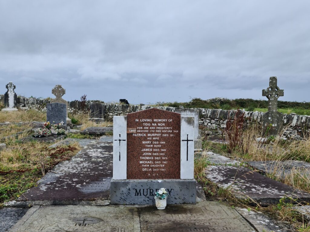 Brown marble headstone flanked with white pillers. Writing read: In loving memory of Tidg na NOR for him and prosterity [sic] left Wexford 1798 died Kinturk 1839. Patrick Murphy died 1911. His Wife Mary, died 1966. Their sons James died 1946, John died 1955, Thomas died 1975, Michael died 1982, Their daughter Delia died 1943. RIP