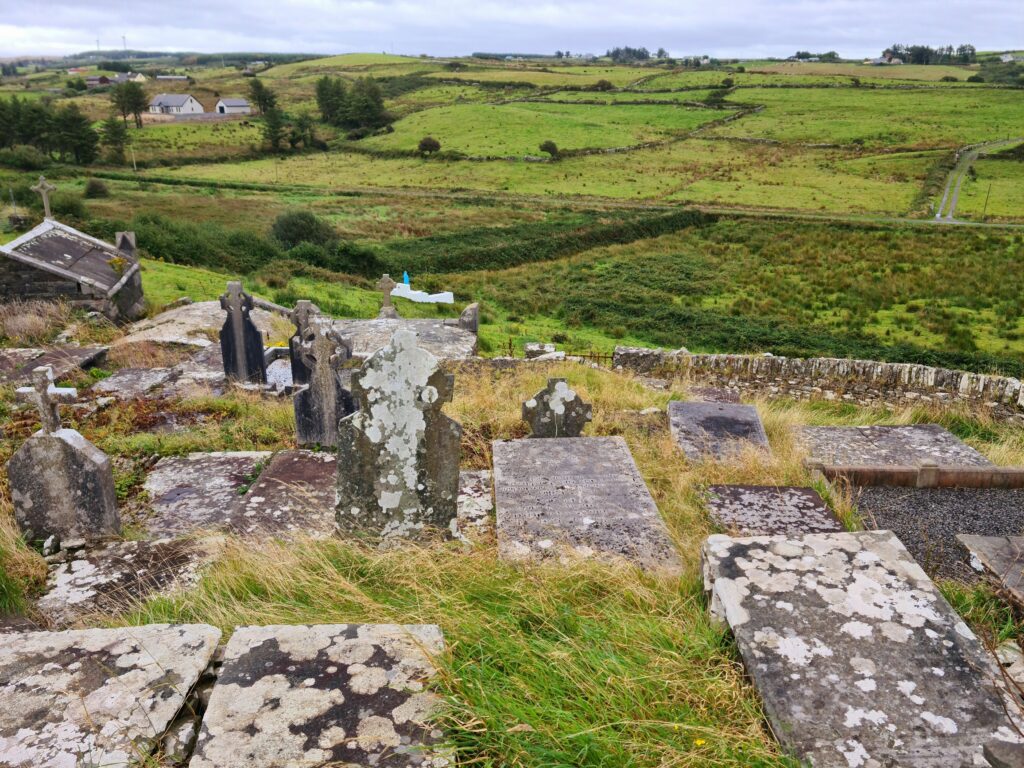 Old graveyard on a hill overlooking fields with sone walls and a few houses in the far distance