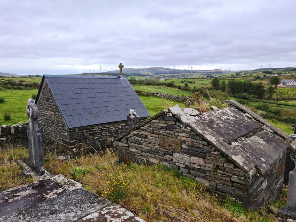 Two gabled tombs on a hill - the one on the left has a new slate roof. The one on the righ has grass growing up through the hole in its roof