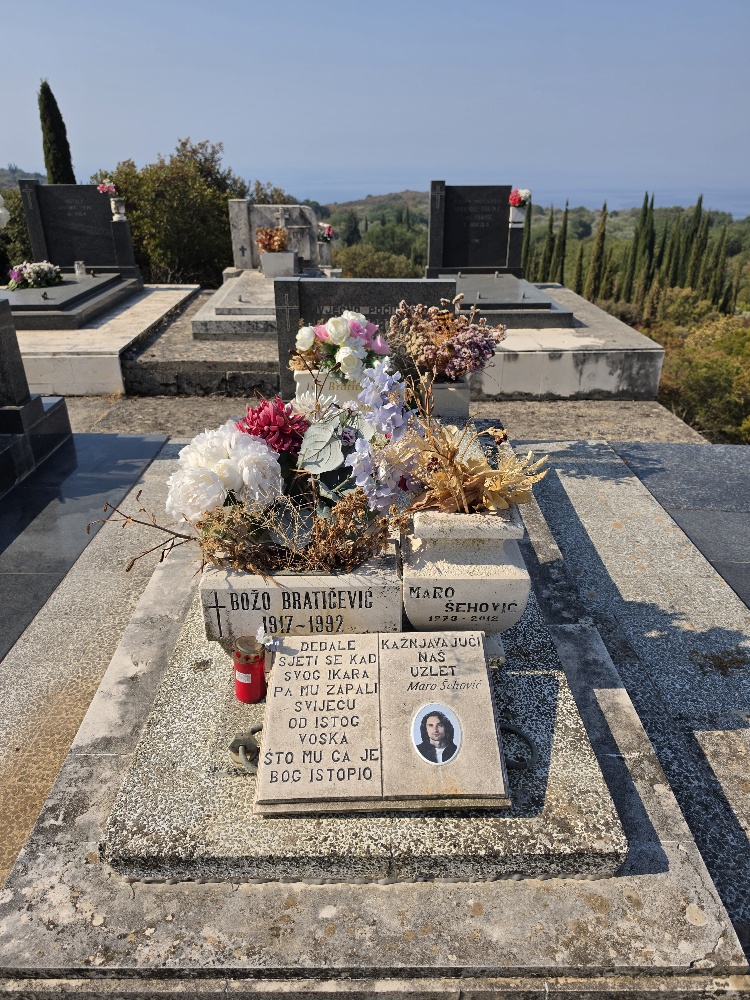 Marble grave of Croatian poet and sculptor Maro Šehović (1973–2012) in the cemetery at Vitaljina, Konavle. The monument is decorated with flowers and bears a photograph of Šehović alongside a poetic inscription invoking Daedalus and Icarus.