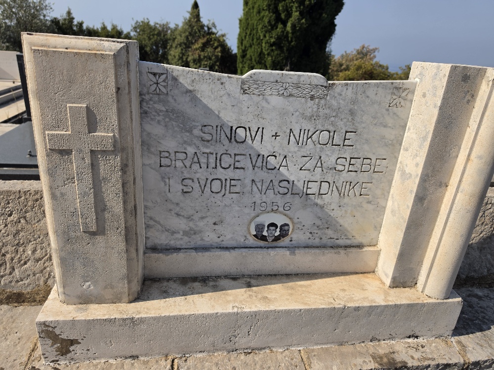 Marble and stone family tomb in the Vitaljina cemetery bearing a Croatian inscription reading “Sinovi Nikole Bratičevića za sebe i svoje nasljednike, 1956,” with a carved cross and floral decoration.