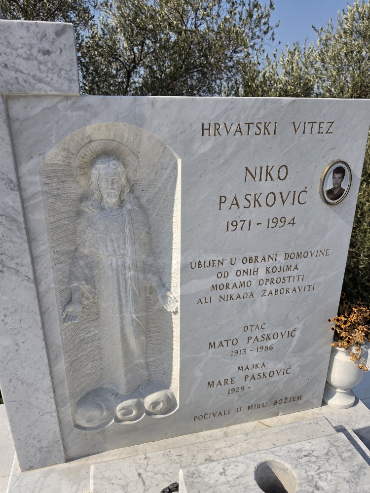 Marble grave monument for Niko Pasković, 1971–1994, in Vitaljina cemetery. The inscription identifies him as a Croatian defender killed defending the homeland and includes a carved image of Christ and his parents' names.